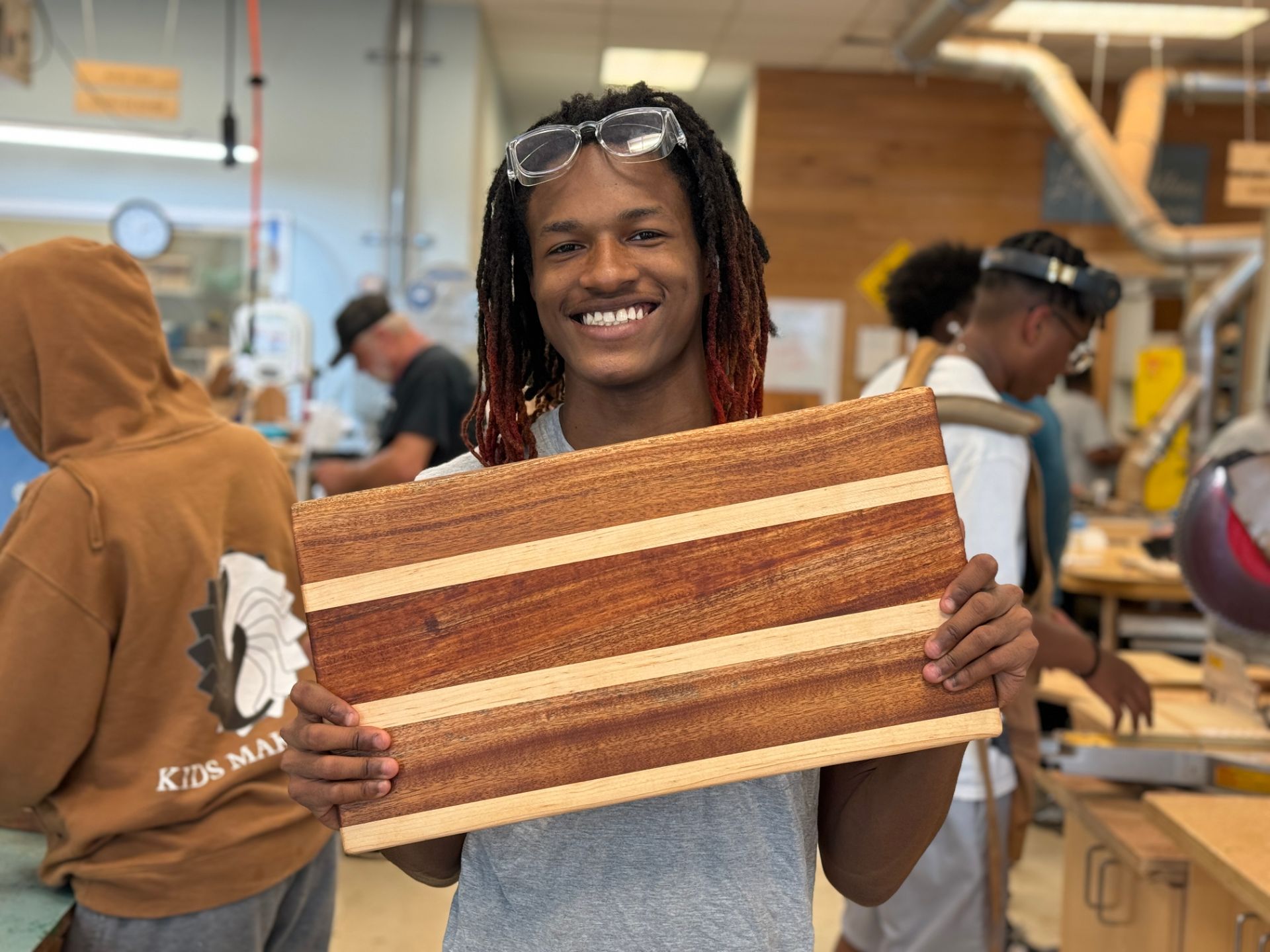 Beaming with pride, a teen holds up the cutting board he built with his own hand
